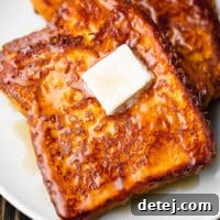 Close-up of a slice of fluffy vegan pumpkin French toast on a white plate, elegantly topped with a square of vegan butter and a drizzle of maple syrup.