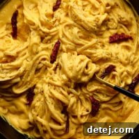 A square image depicting long pasta noodles generously coated in a smooth, creamy yellow butternut squash pasta sauce.