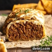 A side view of a perfectly baked and sliced vegan Wellington, revealing its rich, meaty filling wrapped in flaky puff pastry, presented on parchment paper.