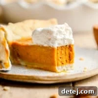 A slice of rich vegan pumpkin pie with a bite removed, garnished with a generous dollop of vegan whipped cream, indicating its creamy texture.