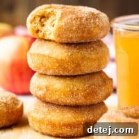 A stack of perfectly glazed vegan apple cider donuts with a glass of apple cider in the background, exuding warm autumn vibes.