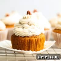 A close-up side view of a beautifully frosted vegan pumpkin cupcake with maple pecan frosting, adorned with chopped pecans on top.