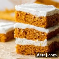 Three perfectly stacked vegan pumpkin cake bars, showcasing their fluffy texture and creamy frosting.