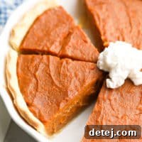 A square image of a baked vegan sweet potato pie, perfectly cut into slices in its pan, revealing its smooth, golden-brown top.