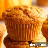 A close-up shot of a perfectly baked, golden-brown vegan pumpkin muffin, revealing its moist texture and inviting spices.