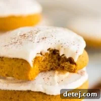 A close-up of a perfectly baked vegan pumpkin cookie with a bite taken out, showcasing its soft texture and creamy frosting.