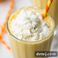 A close-up of the top of a creamy vegan pumpkin milkshake, crowned with whipped cream and a colorful straw, ready for sipping.
