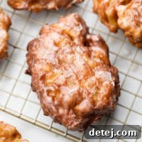 A close-up of a golden-brown vegan apple fritter resting on a cooling rack, showcasing its irregular shape and crispy exterior.