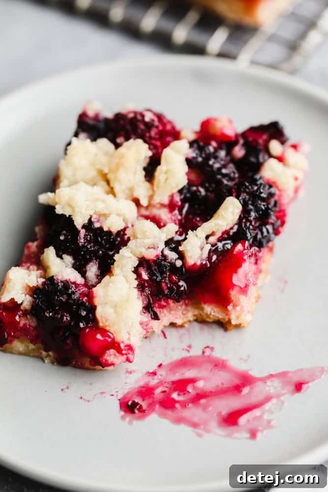 Close-up of a vegan blackberry pie bar on a grey plate, with a bite taken out, revealing the juicy blackberry filling and crumbly topping.