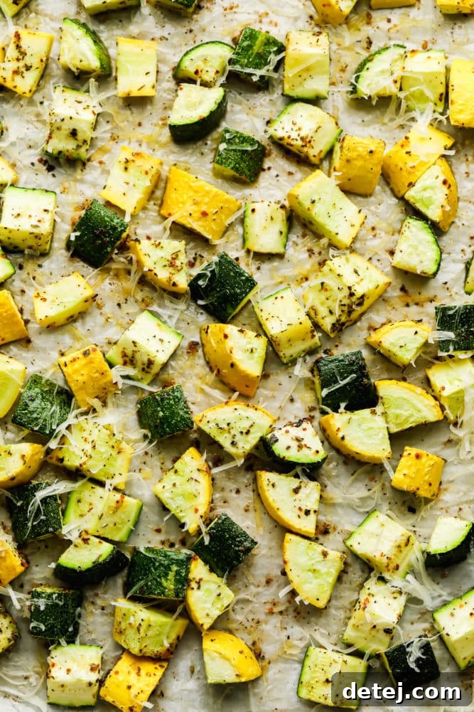 Lots of roasted chunks of squash and zucchini on a parchment-lined pan with cheese on top