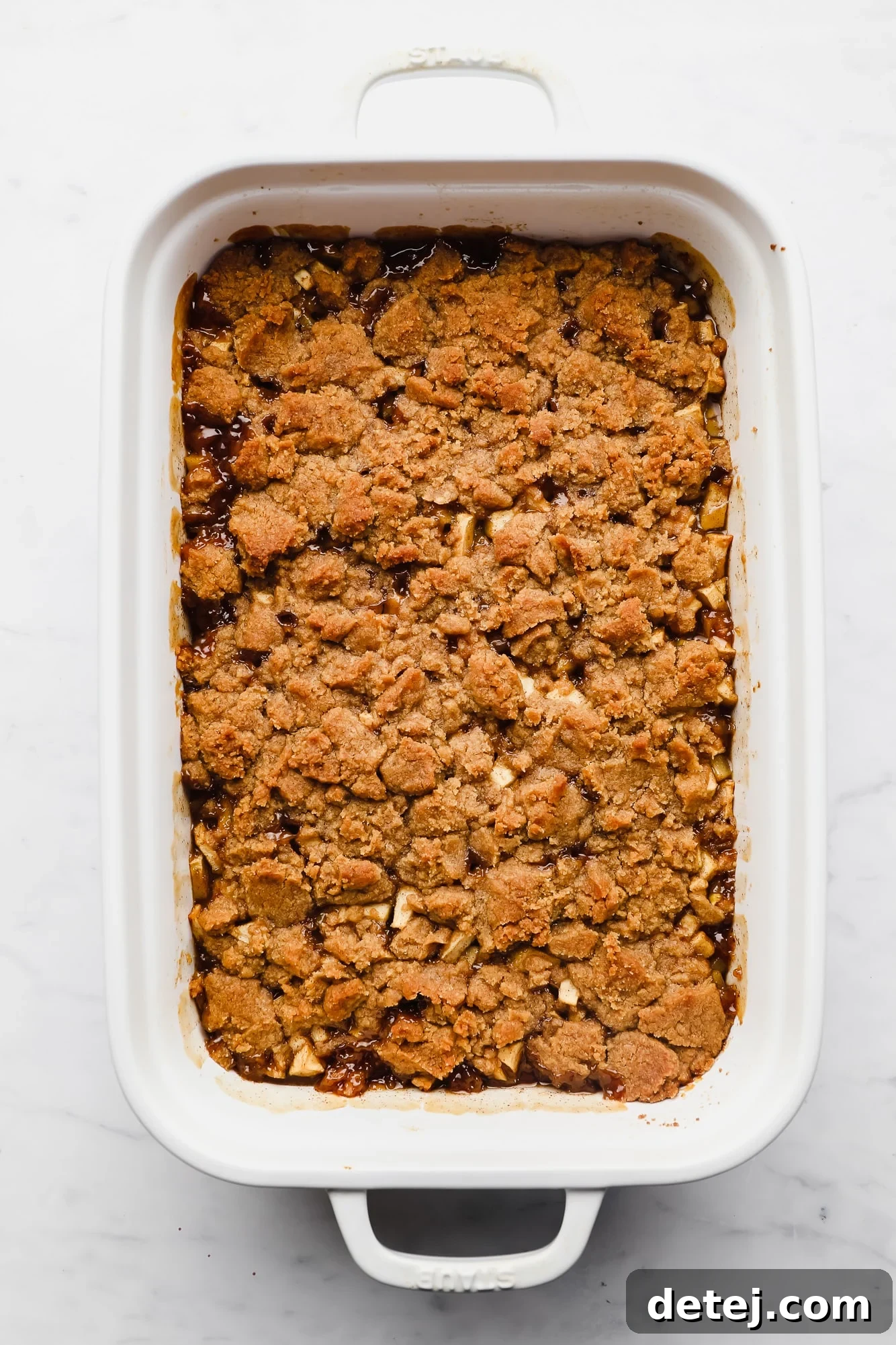 Freshly baked vegan apple crumble with a golden-brown, bubbly streusel topping, hot out of the oven in a large white casserole dish.