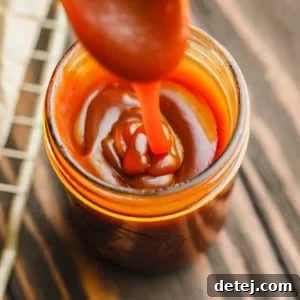 glass jar with caramel sauce drizzling into it from a spoon.