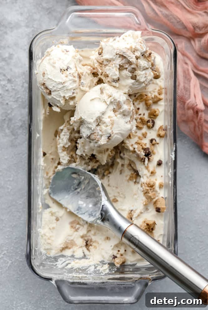 Looking down on a glass loaf pan filled with smooth, white dairy-free cookie dough ice cream, set against a subtle grey backdrop. Chunks of vegan cookie dough are visible throughout.