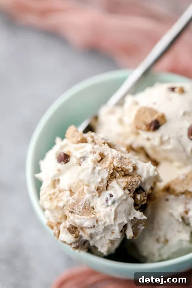 A vibrant teal bowl holds generous scoops of dairy-free ice cream, speckled with pieces of vegan cookie dough, all placed on a sleek grey background.