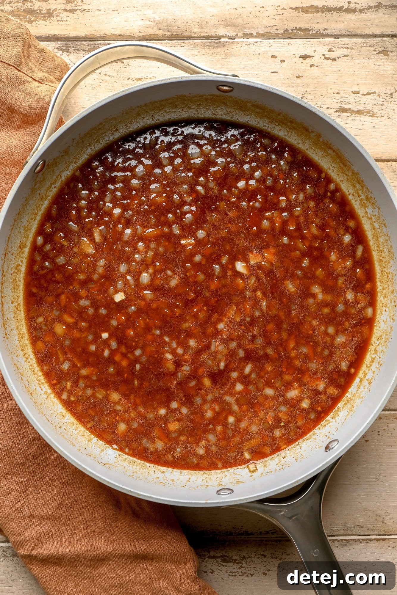A vibrant red, thick barbecue sauce simmering in a skillet, ready to be combined with beans for the ultimate vegan baked beans.