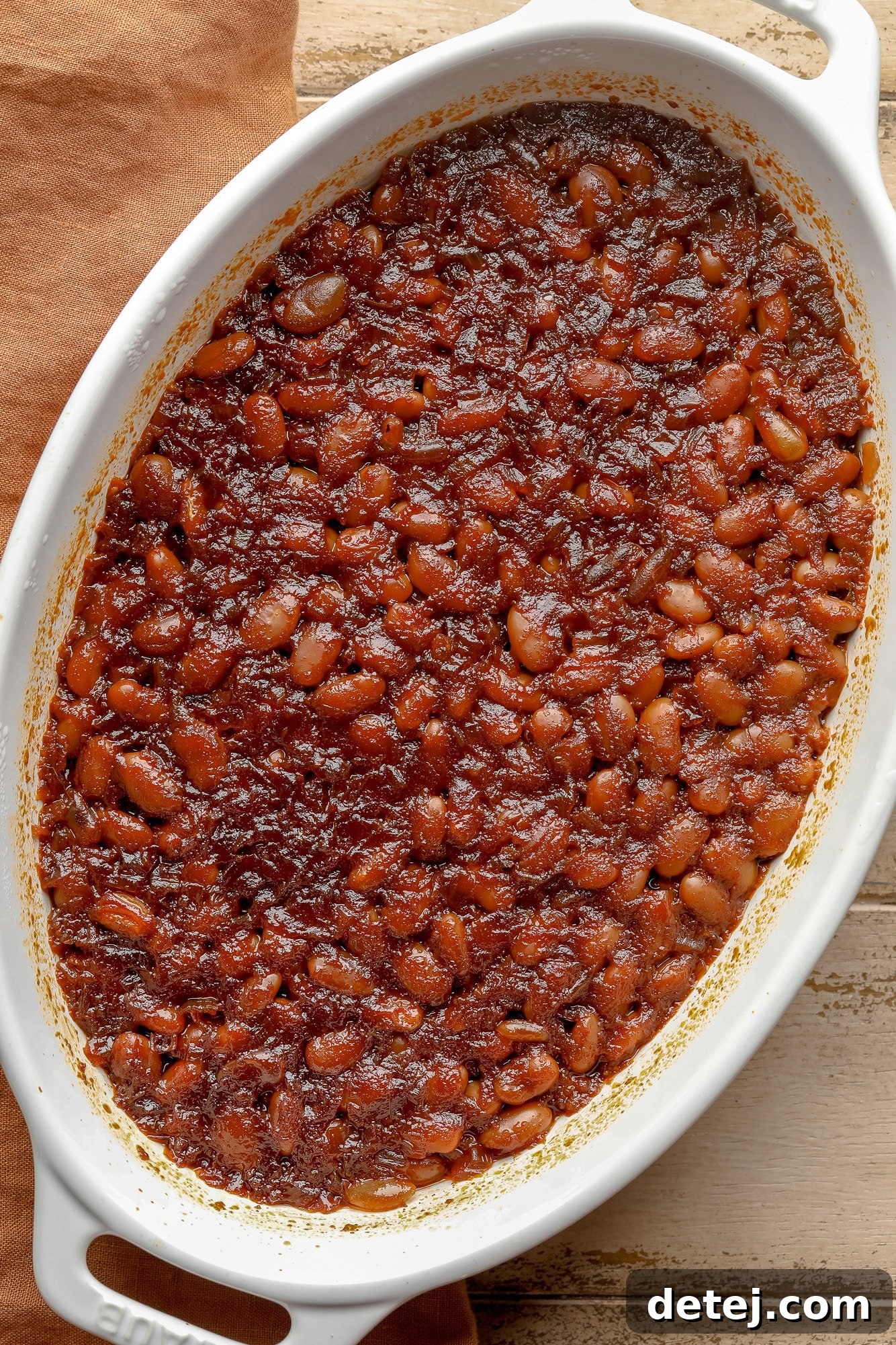 A bubbling casserole dish filled with perfectly cooked vegan baked beans, the rich sauce thickened and caramelized on top, straight from the oven.