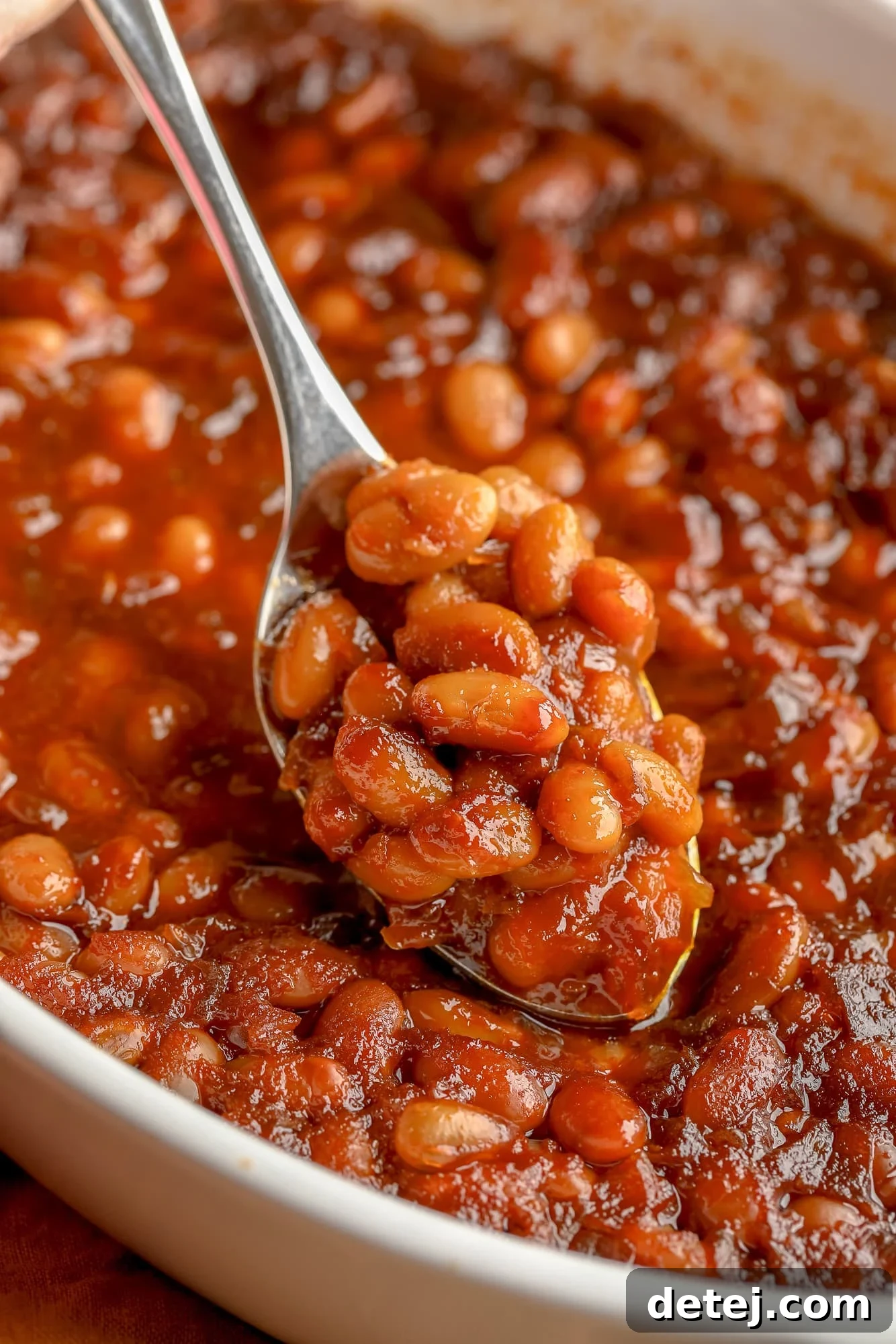 A close-up shot of a spoon filled with delicious vegan baked beans, showcasing the rich, thick sauce and perfectly cooked navy beans.