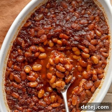 close up on a spoon scooping up a bite of vegan baked beans from a casserole dish.