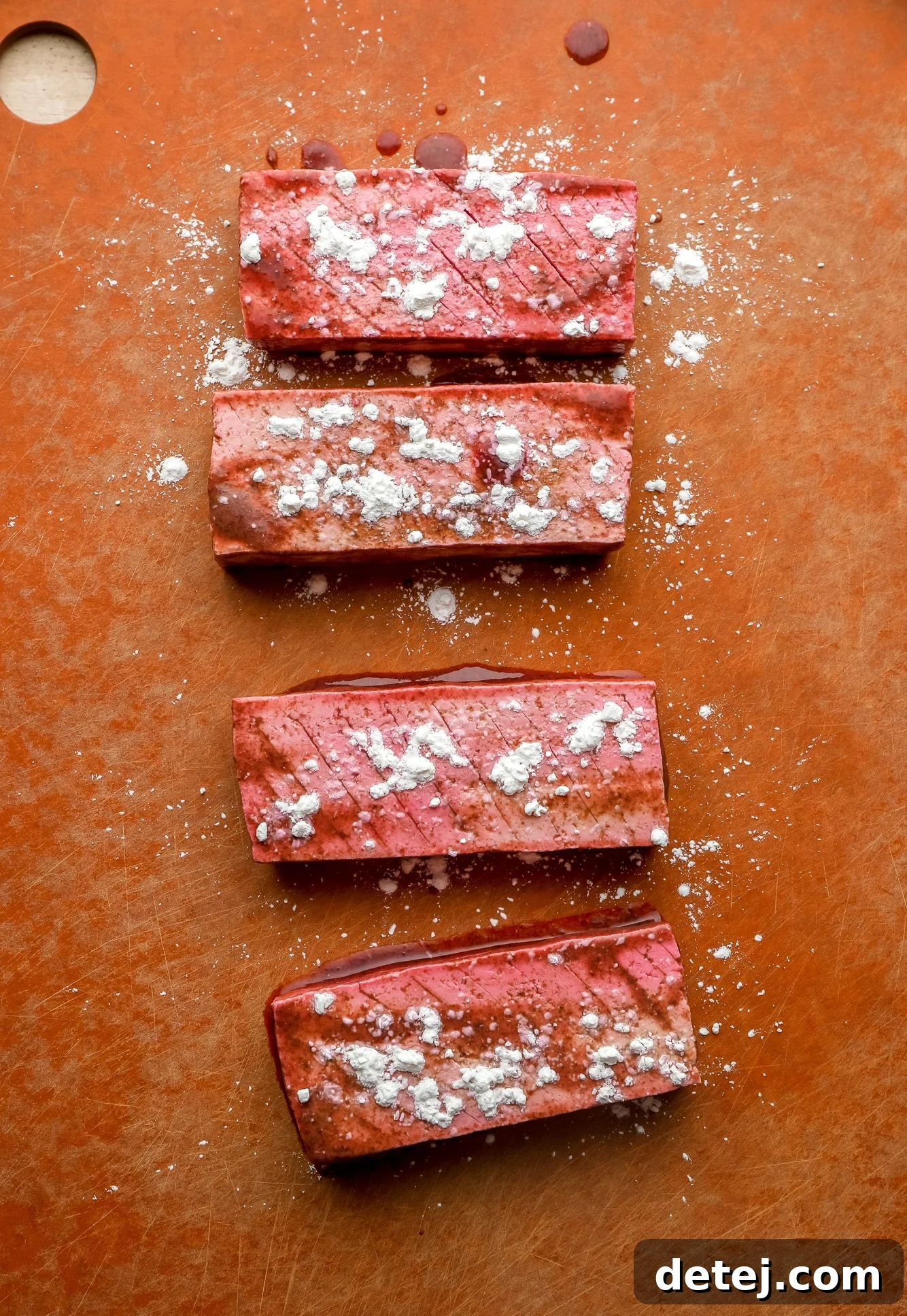 4 pieces of vegan salmon with cornstarch sprinkled on top on a red cutting board.