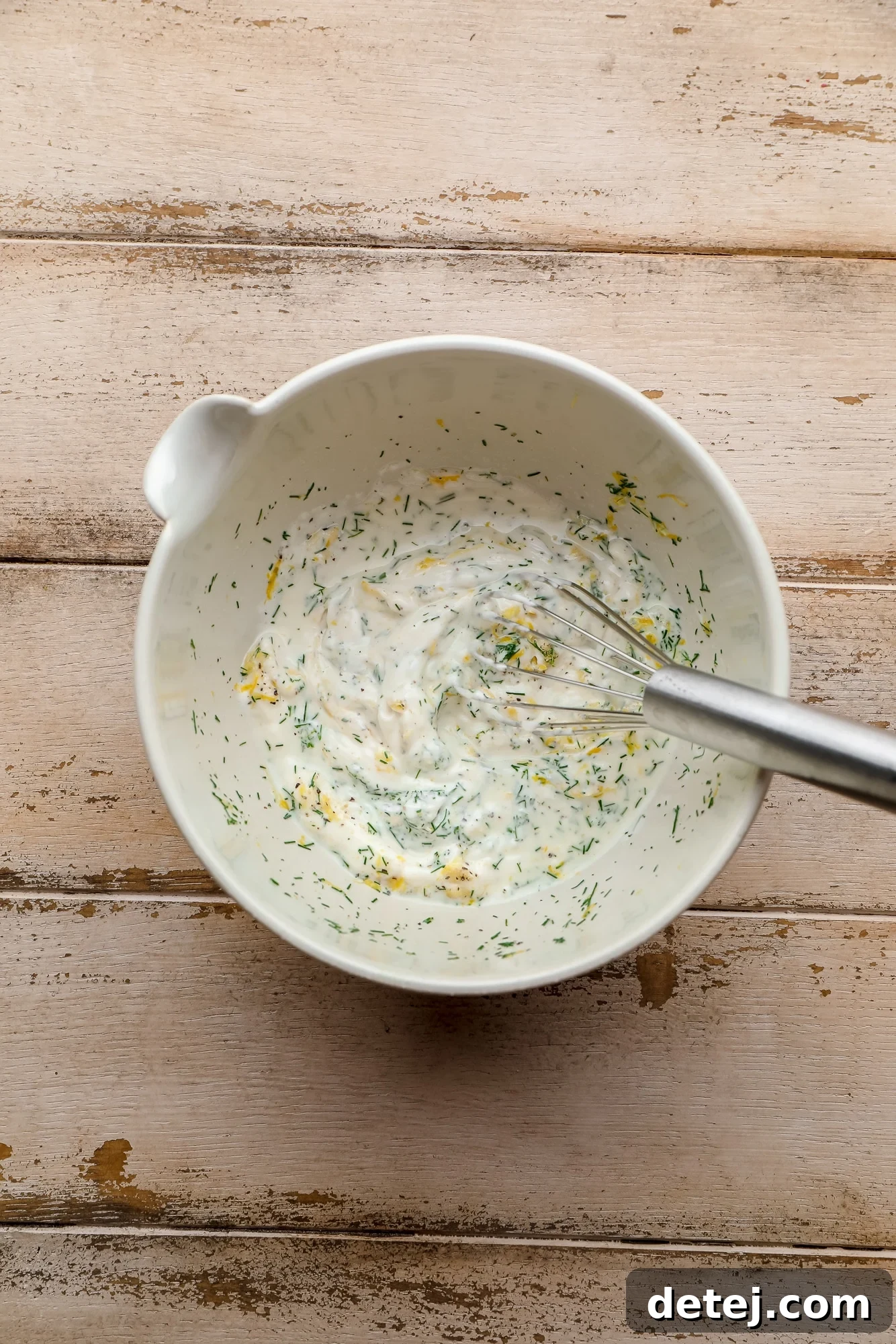 whisking lemon dill sauce ingredients together in a white bowl.