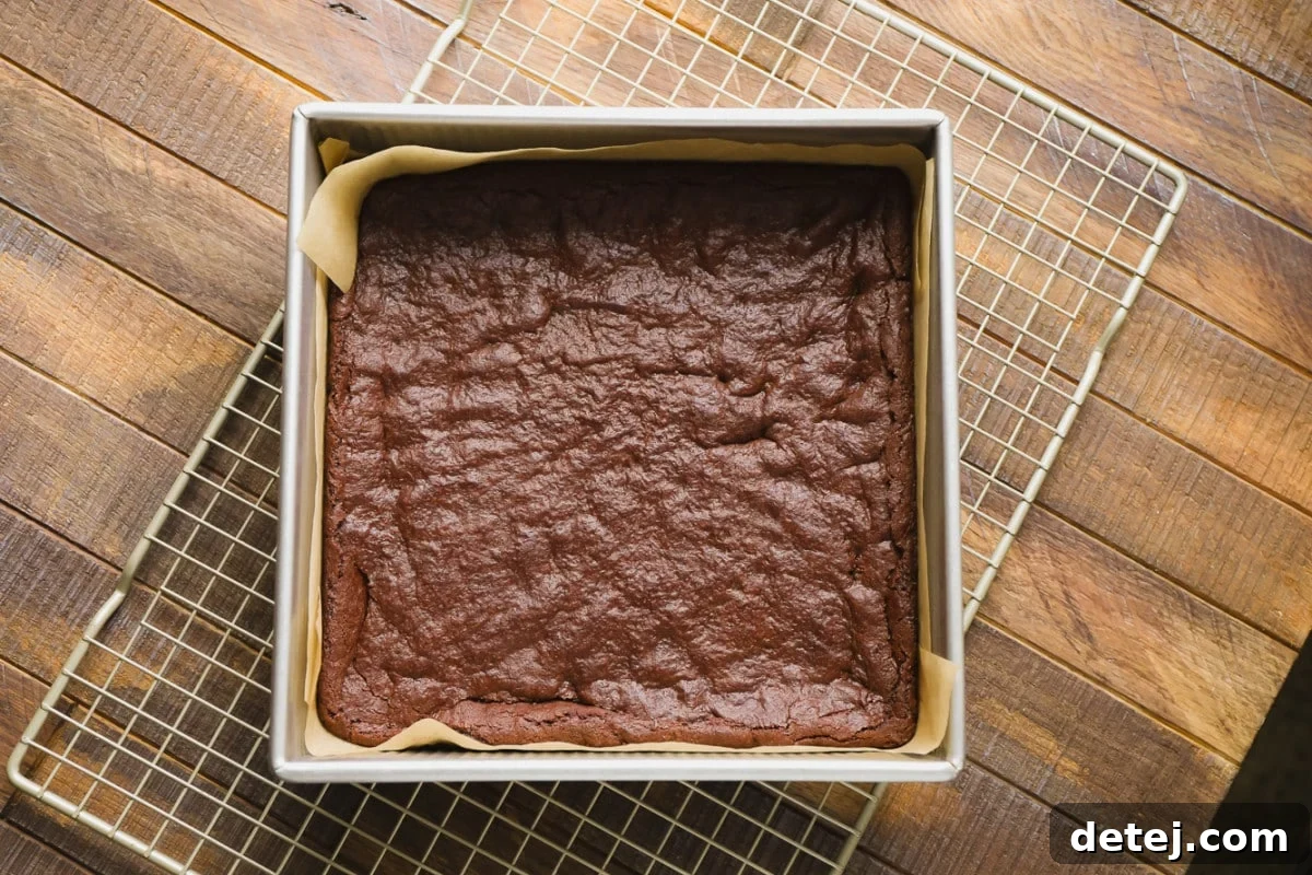 Freshly baked chocolate brownies in a square pan, resting on a rustic wooden background, ready for the next delicious layers.