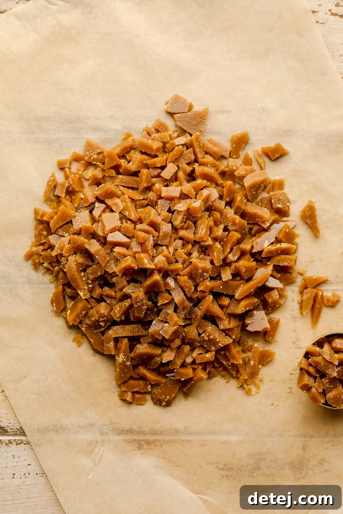 A collection of small, irregular vegan toffee bits, without chocolate, scattered on a piece of parchment paper, ready for baking.