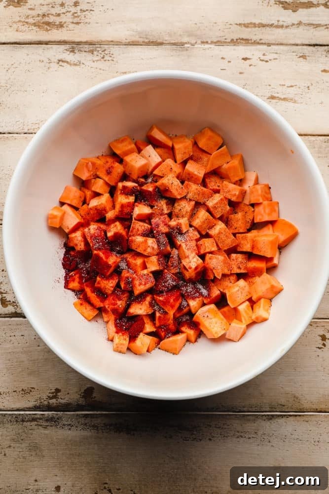 white bowl full of raw chopped and peeled sweet potatoes and spices on wood background.