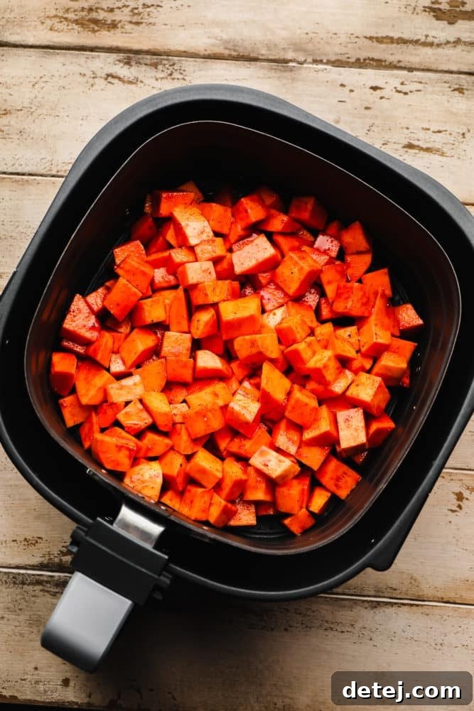 uncooked sweet potatoes chopped in an air fryer on wood background.