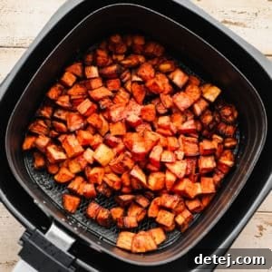 black air fryer with cooked sweet potato chunks in it.