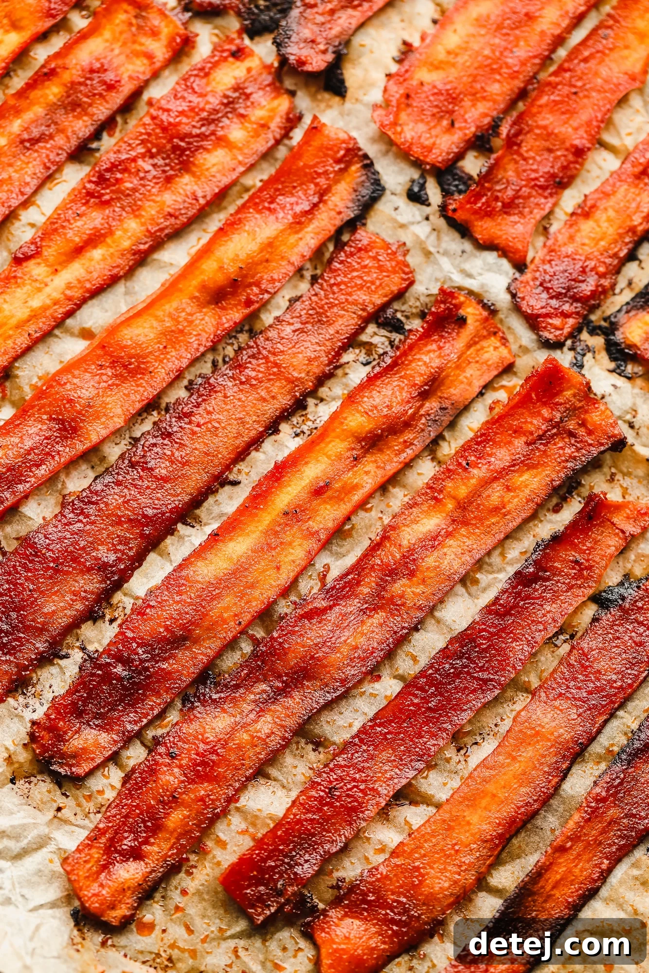 close up on strips of vegan bacon laying on a parchment-lined baking sheet.