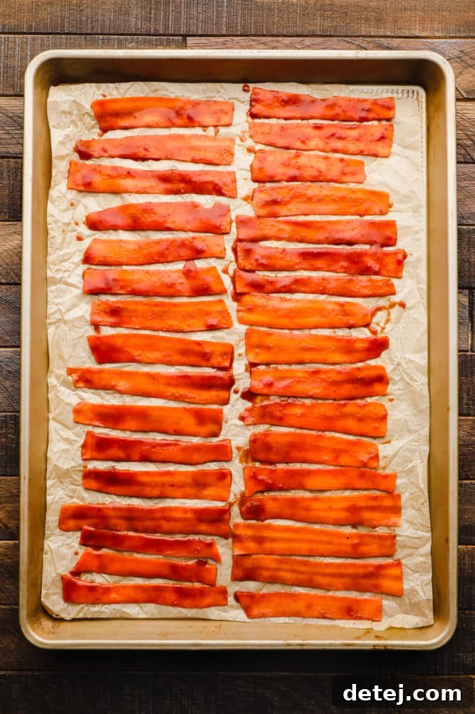 rows of marinated carrot strips on a parchment lined baking sheet.
