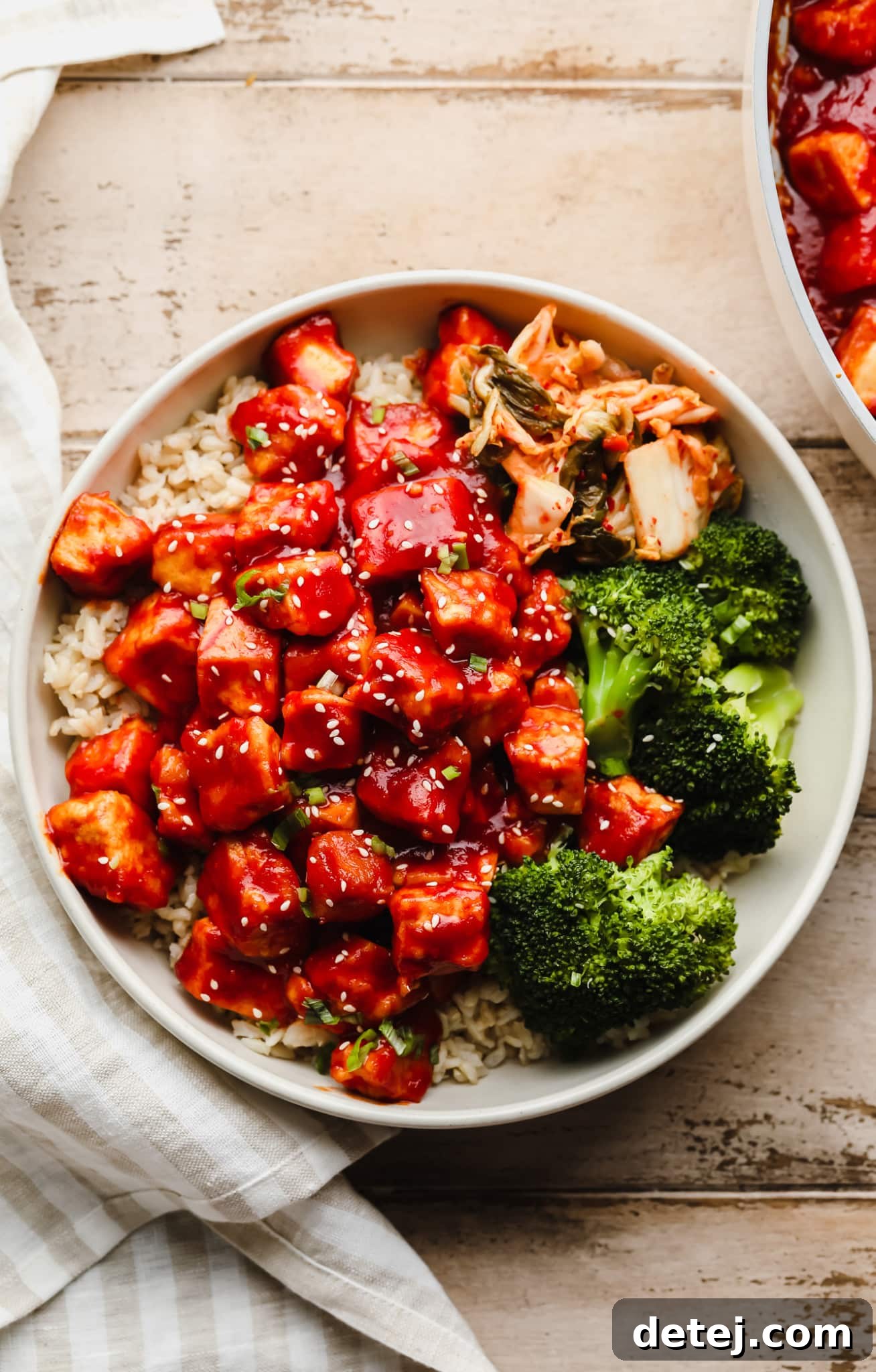 Gochujang Tofu in a white bowl with rice, broccoli, and kimchi, garnished with sesame seeds.
