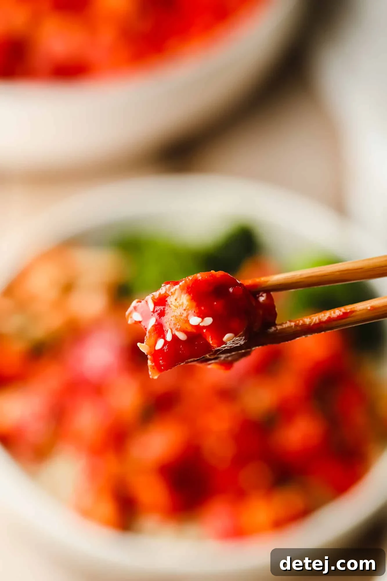 Close up on a piece of Gochujang Tofu held by chopsticks, highlighting the crispy texture and spicy glaze.