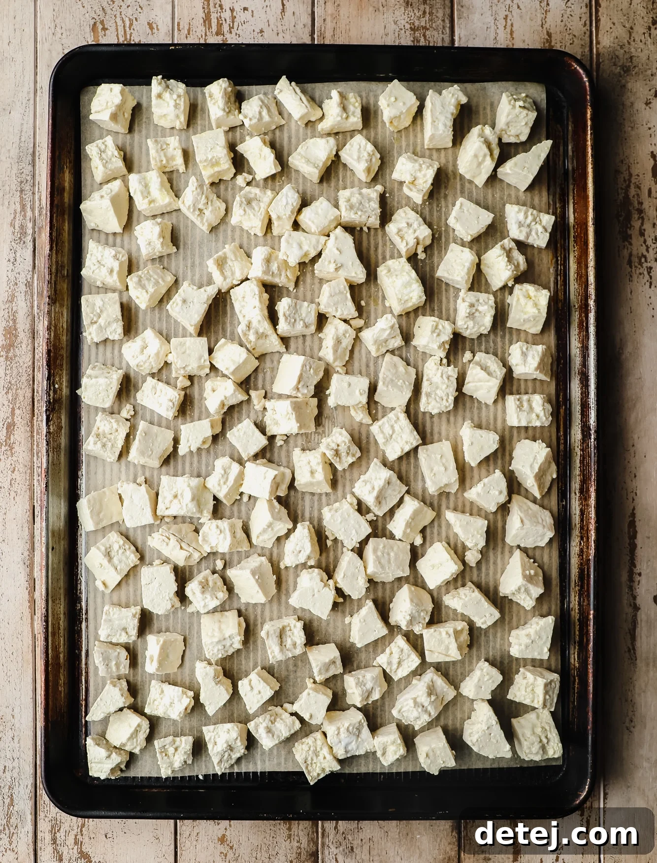 Small, irregularly ripped tofu pieces laying in an even layer on a baking sheet, coated with cornstarch.