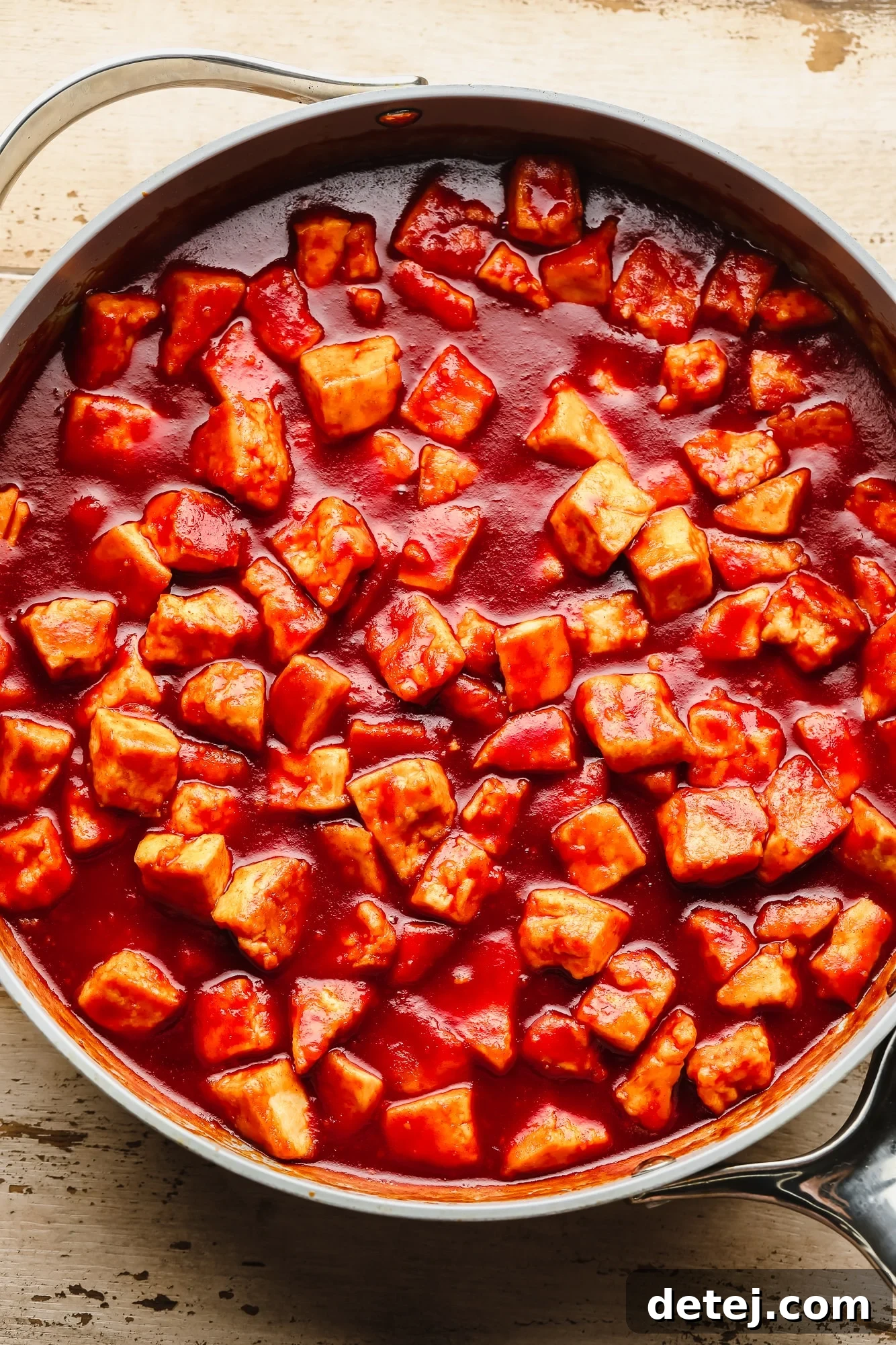 Cooking crispy tofu pieces in a vibrant red Gochujang sauce in a large skillet, with a wooden spoon mixing.