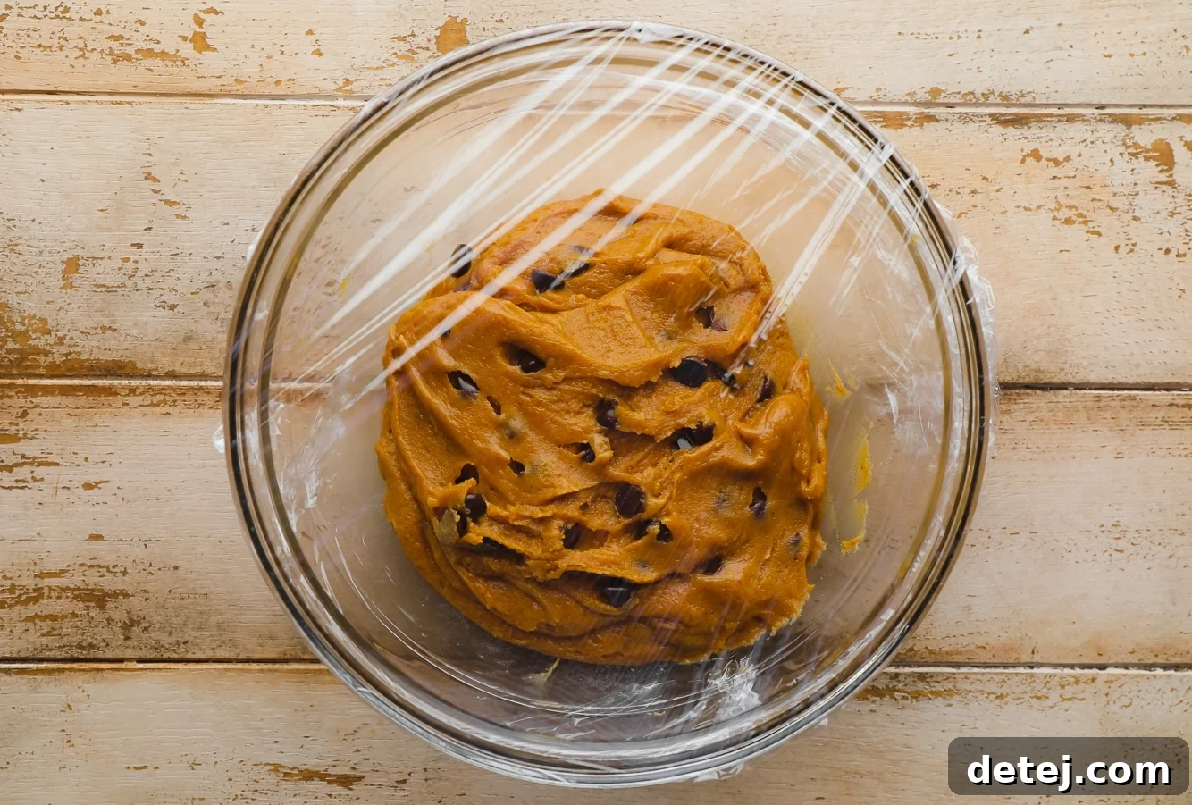 Pumpkin Chocolate Chip Cookie dough in a glass bowl covered with plastic wrap.