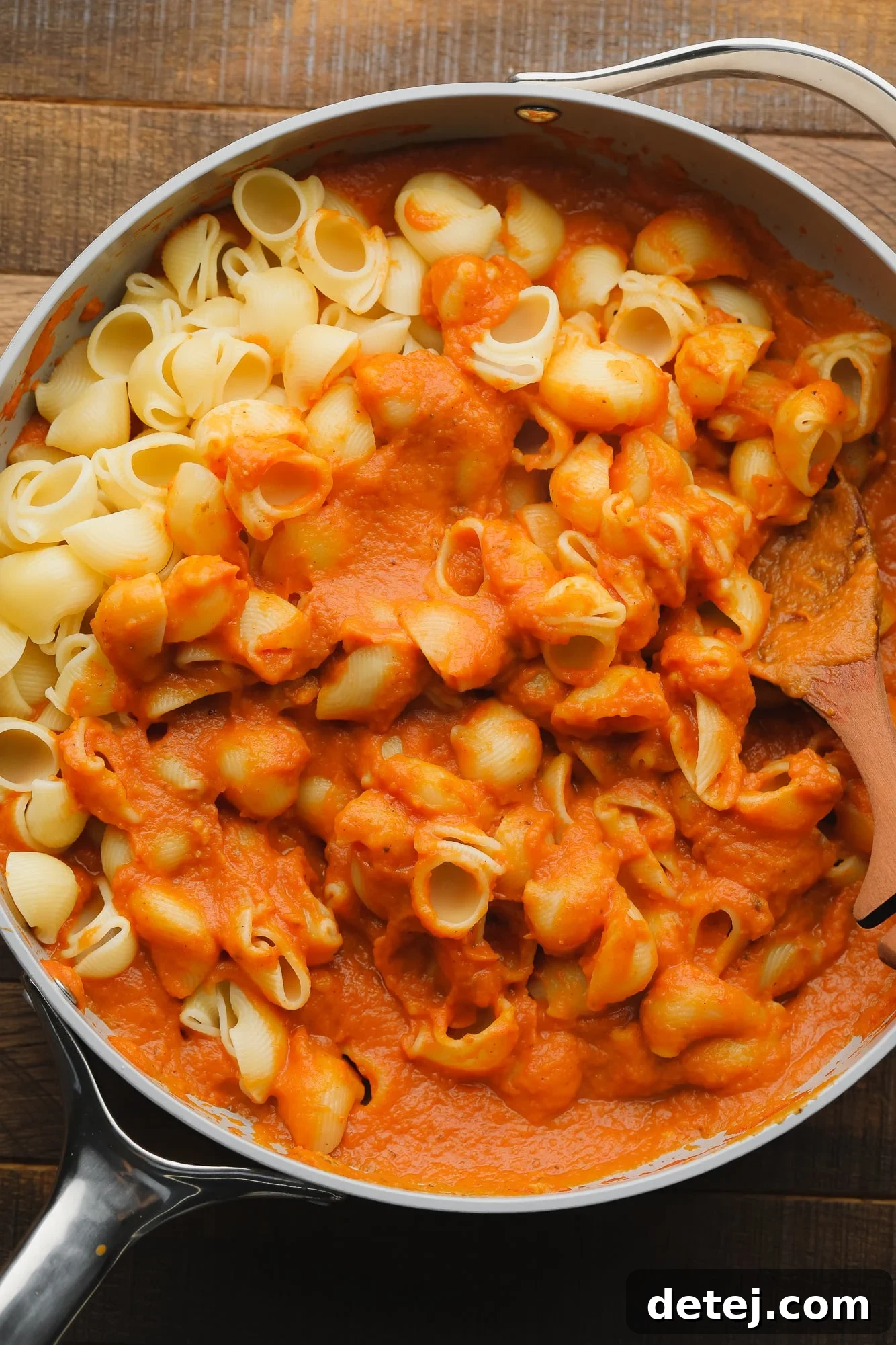 Stirring cooked pasta noodles into a skillet with pumpkin pasta sauce.