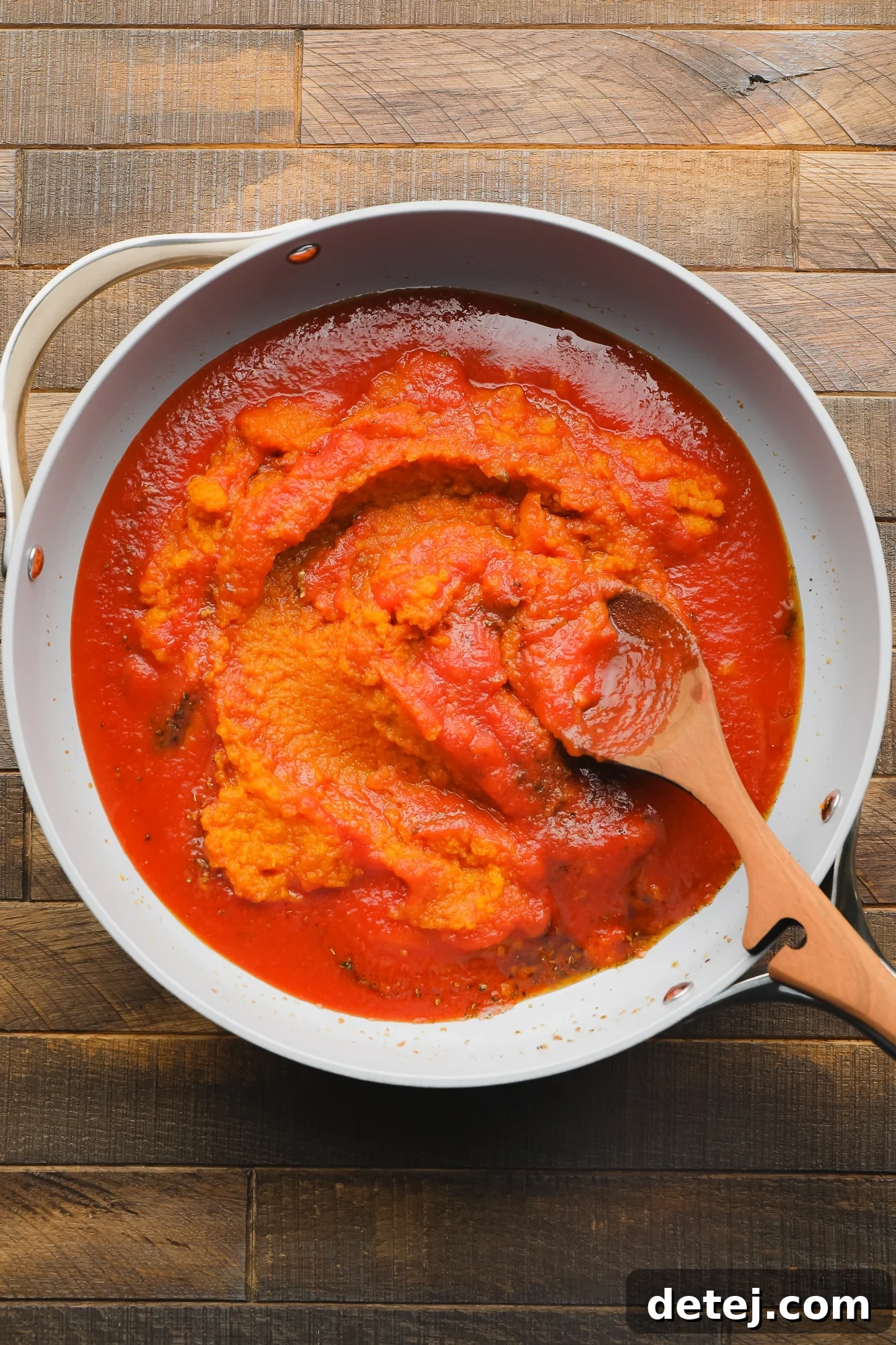 using a wooden spoon to stir pumpkin puree and tomato sauce together in a skillet.