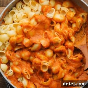 Stirring cooked pasta noodles into a skillet with pumpkin pasta sauce.