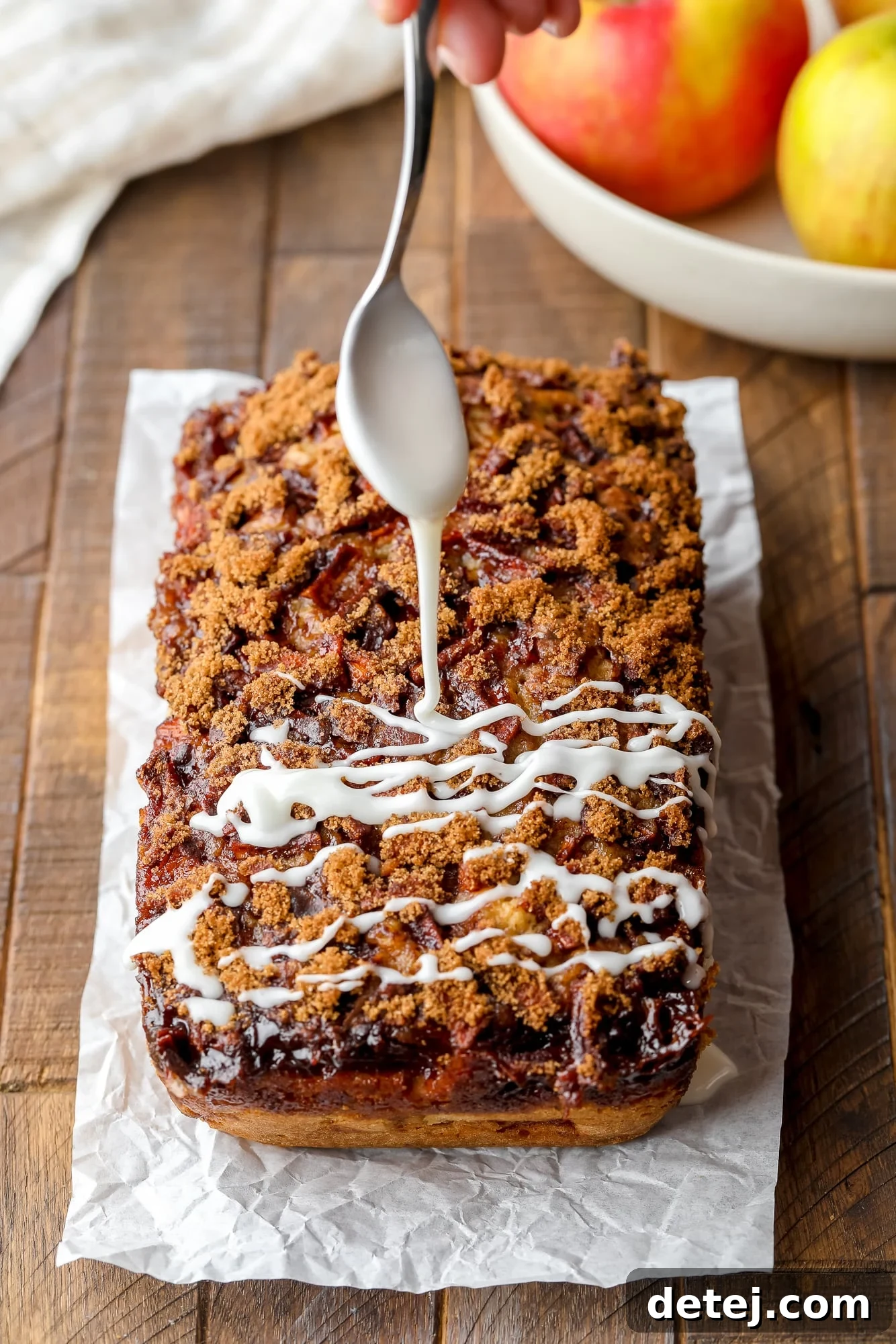 Drizzling a thin, white icing over a loaf of apple fritter bread.