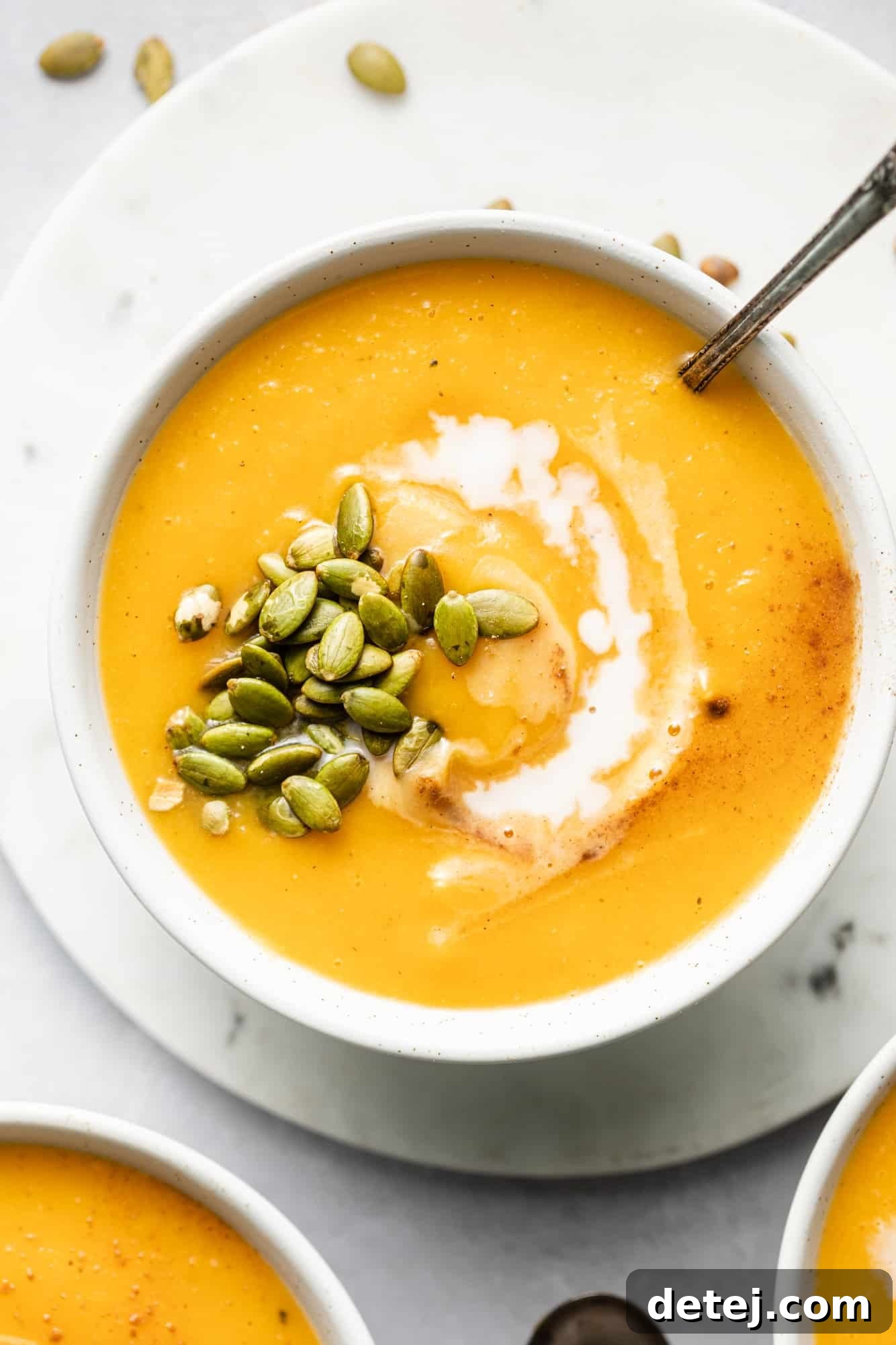 A beautifully presented bowl of creamy vegan butternut squash soup, garnished with a swirl of coconut milk and crunchy pepitas.