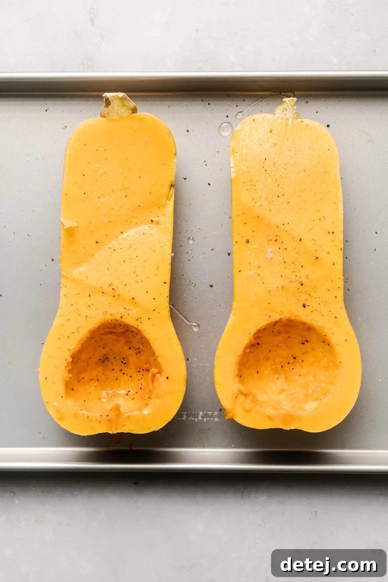 A large butternut squash cut in half lengthwise, with seeds removed, placed on a baking sheet, ready for roasting.