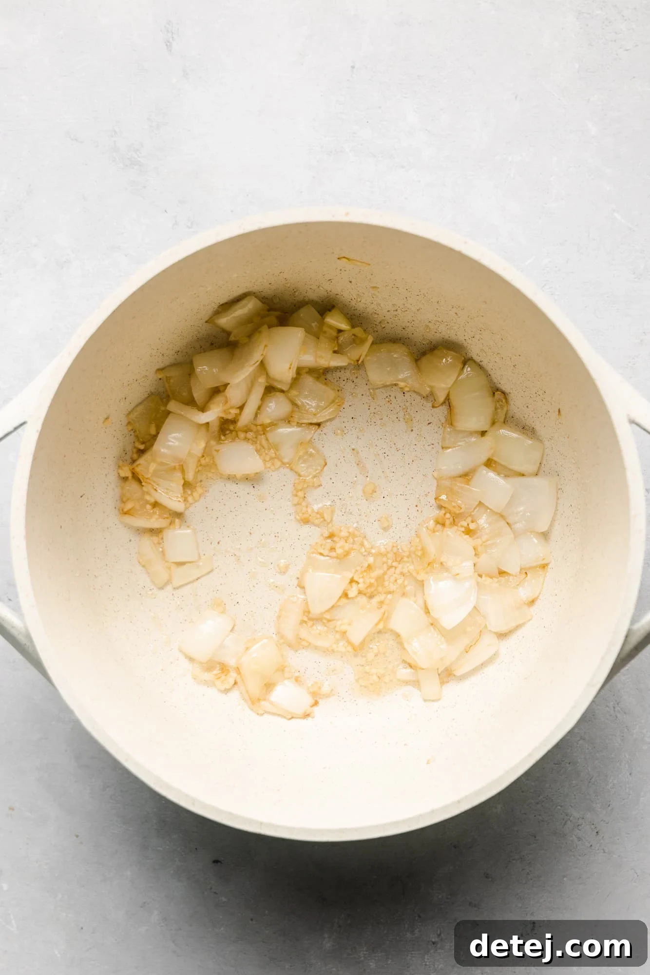 Close-up of cooked onions and minced garlic gently sautéing in a white pot, emitting a fragrant aroma.