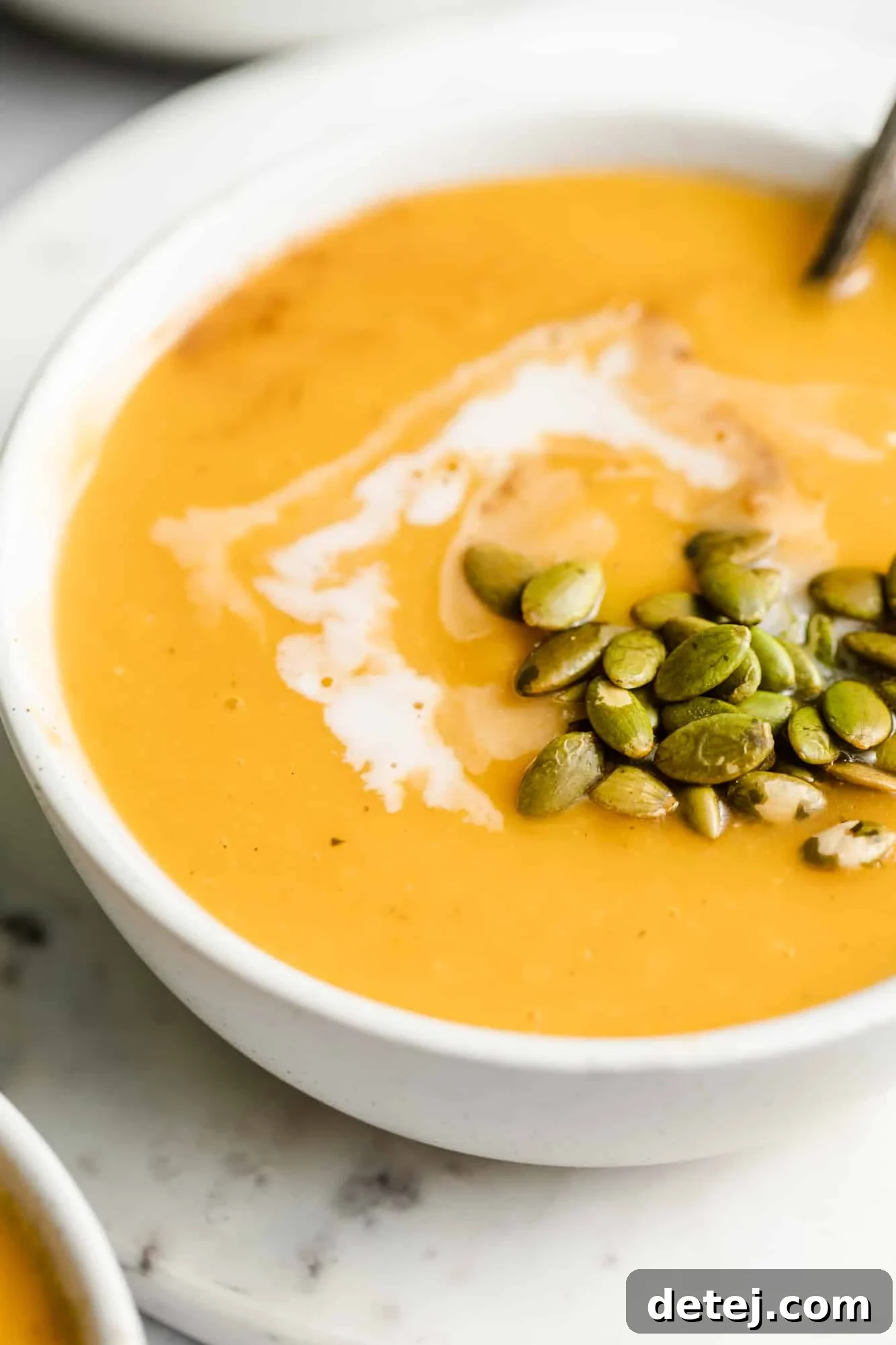 A final, appealing image of a white bowl filled with creamy butternut squash soup, elegantly topped with a swirl of coconut milk and crunchy pepitas.