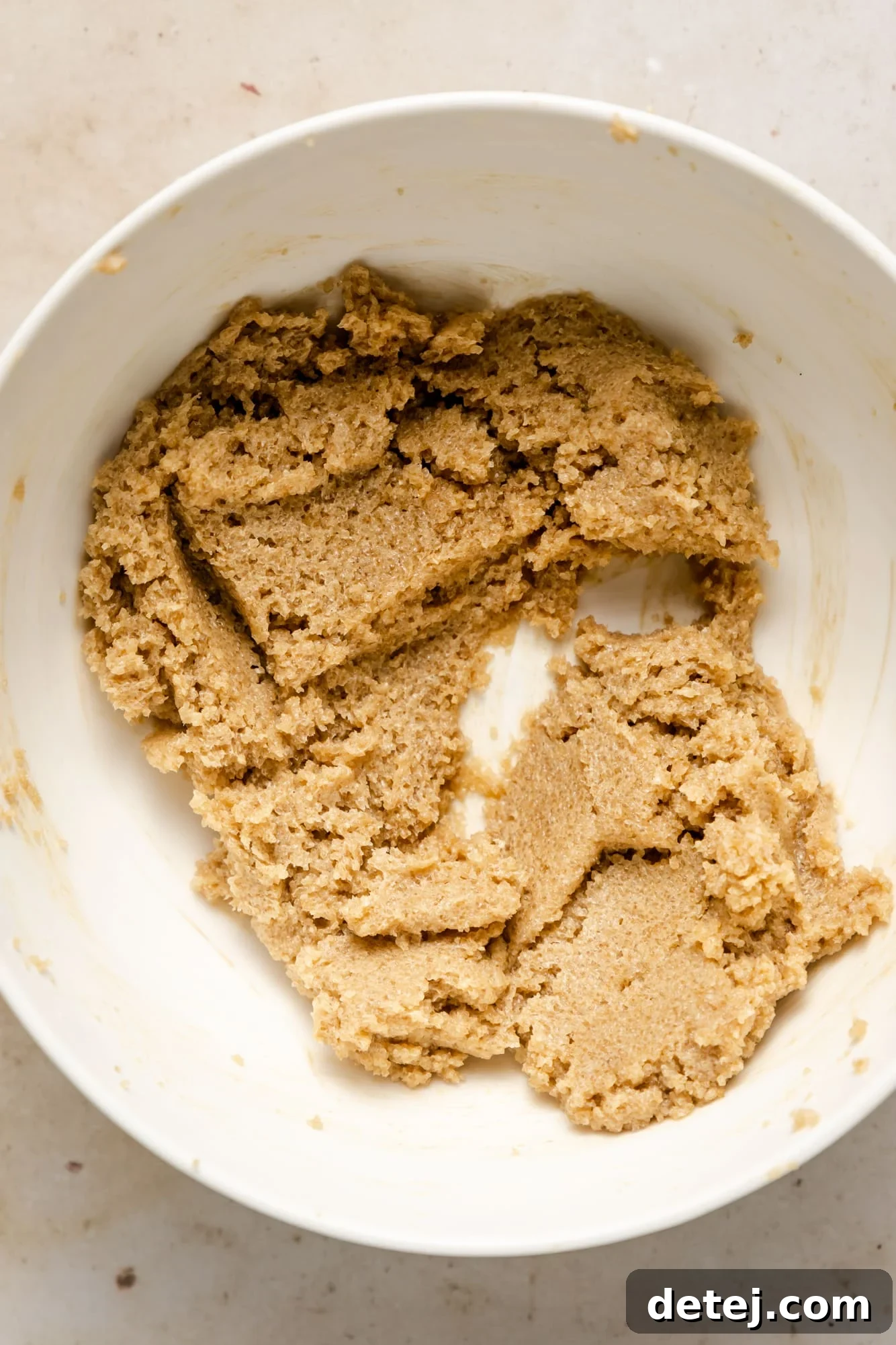 A light brown, raw vegan cookie dough rests in a clean white mixing bowl, awaiting the addition of delicious mix-ins.