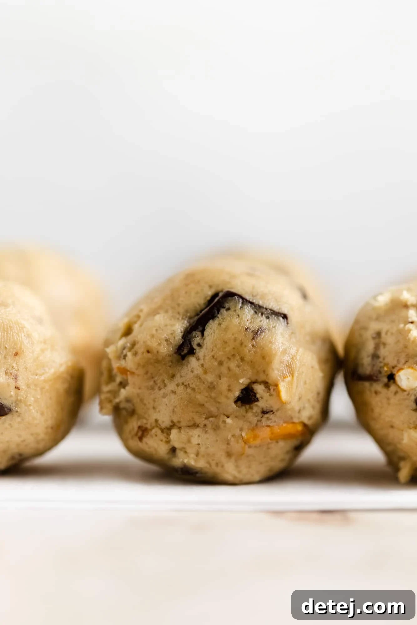 Small, uniformly scooped balls of raw vegan kitchen sink cookie dough are meticulously arranged on parchment paper, perfectly prepared and ready for baking.