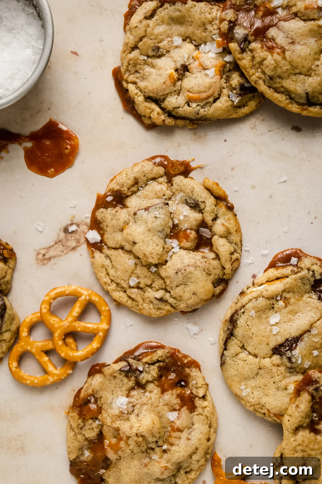 A beautiful display of baked vegan kitchen sink cookies, artfully arranged next to a small bowl of flake salt and a scattering of pretzels, emphasizing their rustic charm and delicious appeal.