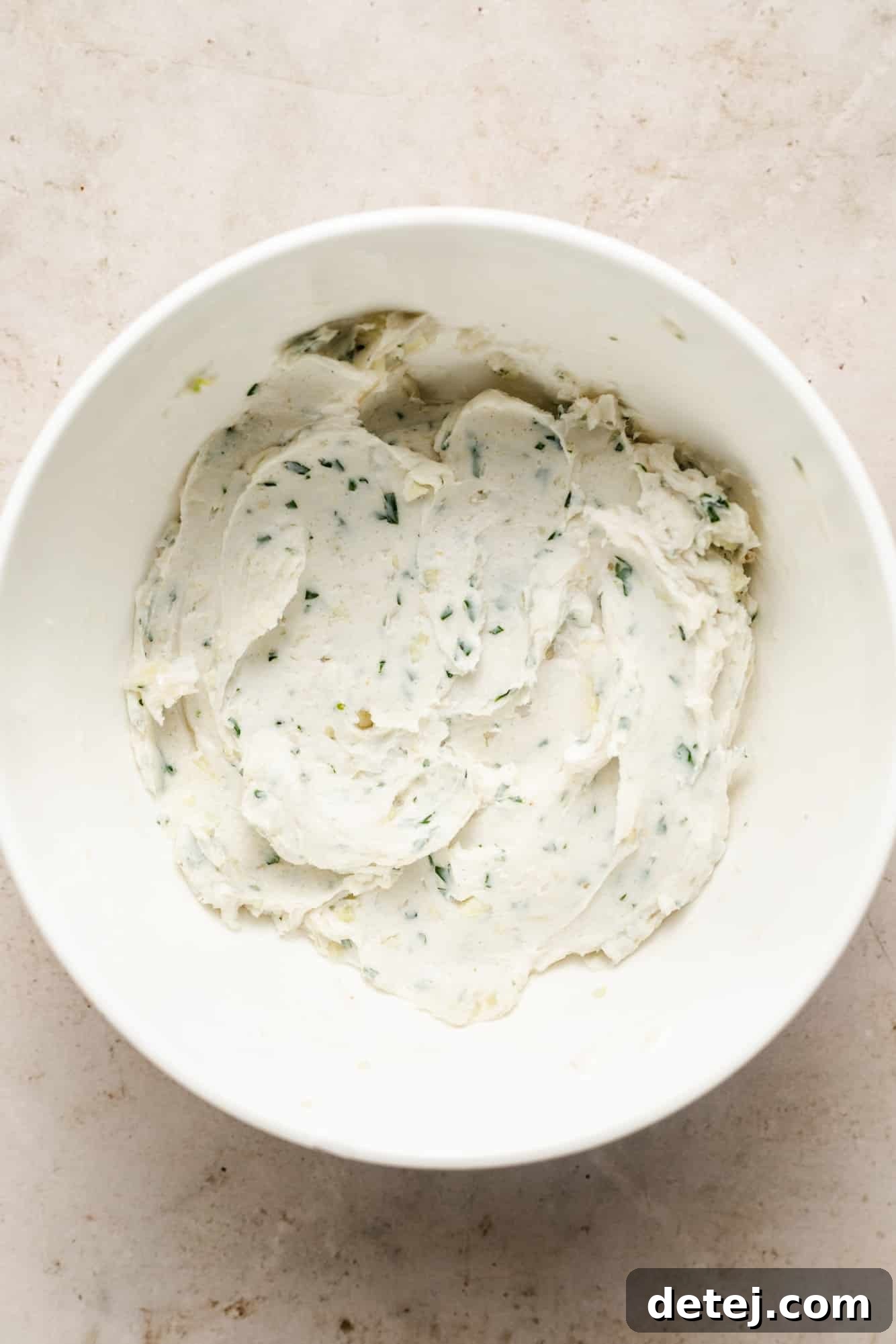 a vegan garlic butter spread with fresh herbs in a white bowl.