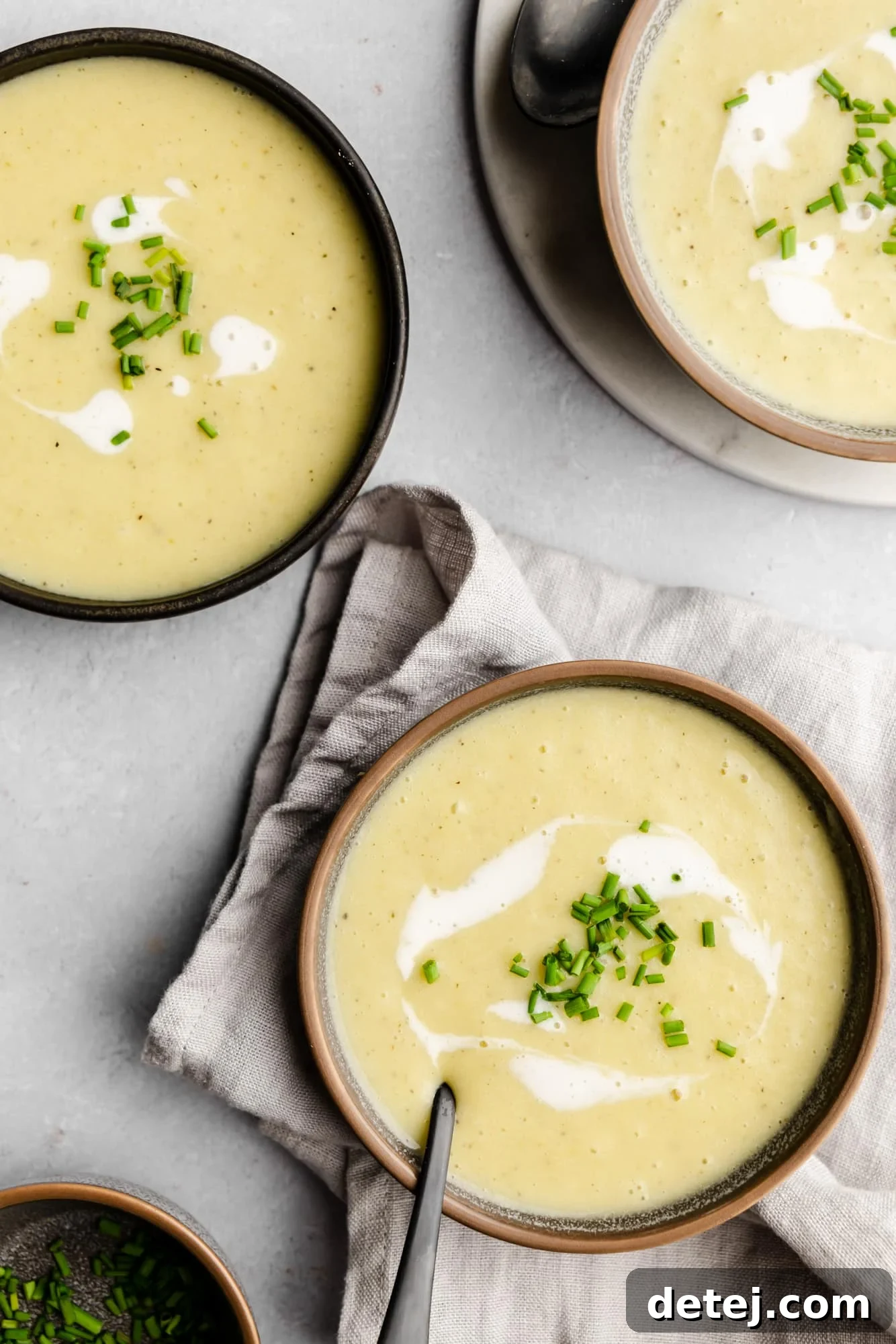 Overhead view of three bowls of creamy Vegan Potato Leek Soup, garnished with a swirl of coconut cream and fresh chives, inviting a comforting culinary experience.
