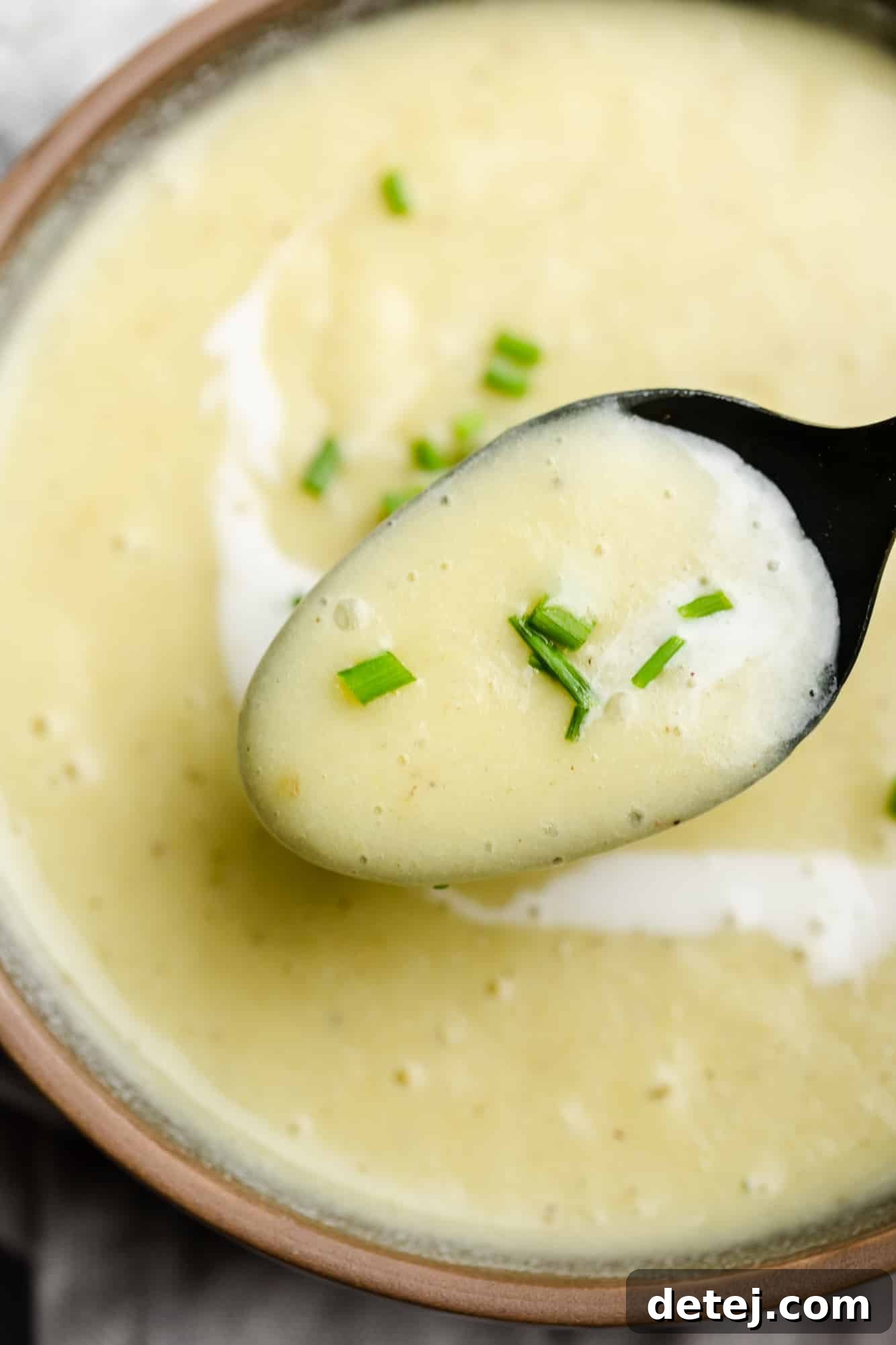 A close-up shot of a spoon lifting a generous scoop of smooth, creamy Vegan Potato Leek Soup from a white bowl, highlighting its rich texture and inviting warmth.